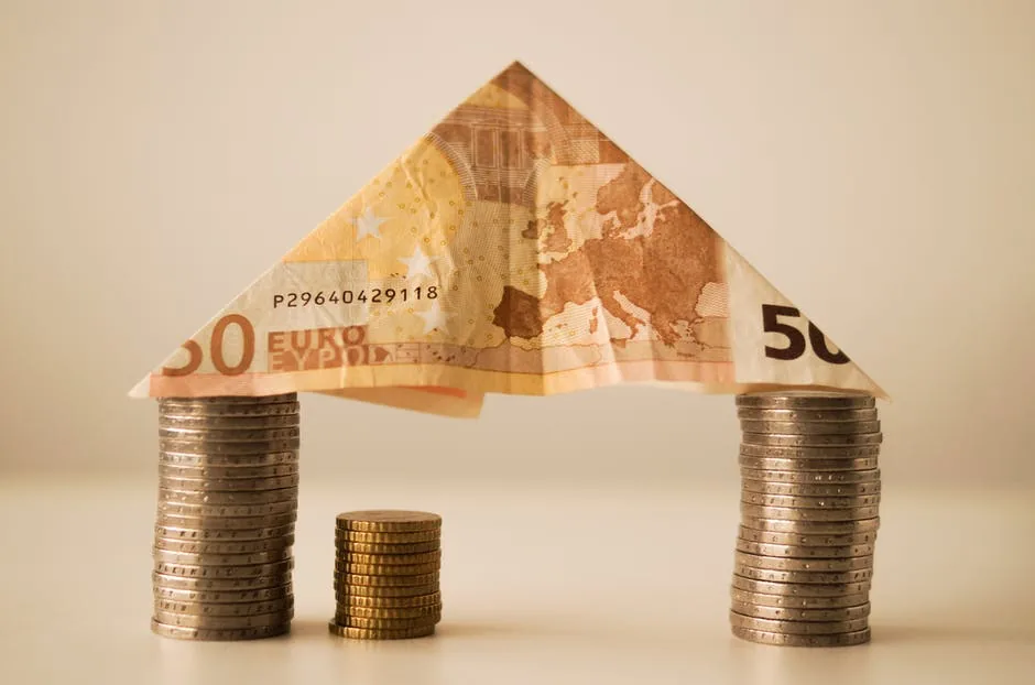 Casa construída com cédulas de euro e moedas, símbolo da relação entre dívida e lucro empresarial