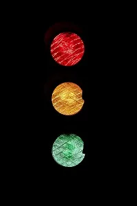 Semáforo com três luzes vermelho amarelo verde em fundo preto ilustrando conceito downsizing