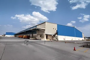 Galpão industrial cinza-azul com estrutura metálica sob céu nublado