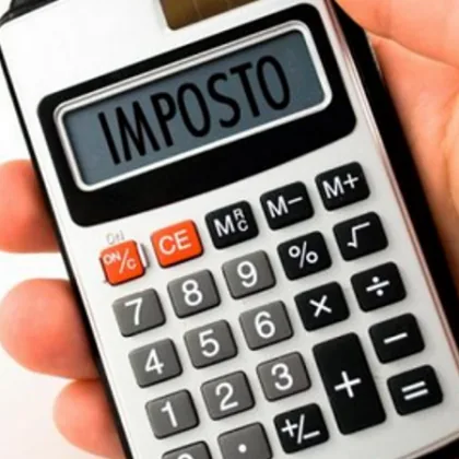 Mão segurando calculadora branca mostrando palavra imposto relacionada à área fiscal o que faz