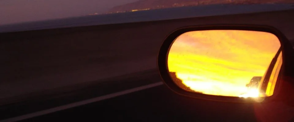 Espelho lateral de carro refletindo luz dourada ao entardecer em visão retrospectiva